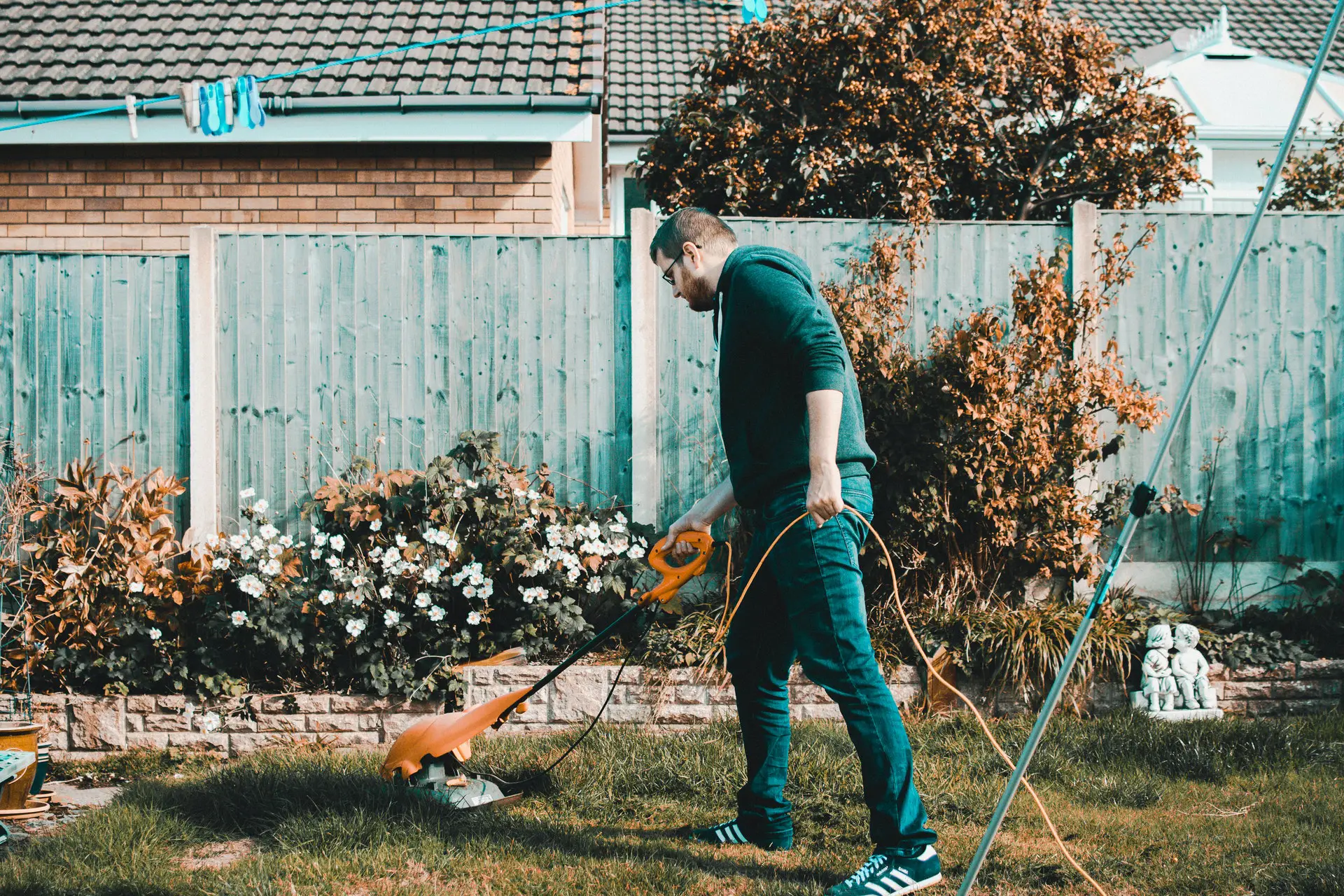 man-holding-orange-electric-grass-cutter-on-lawn-1453499